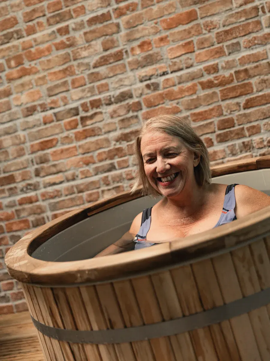 A member laughing up to her shoulders in a cold plunge at Pulse Club